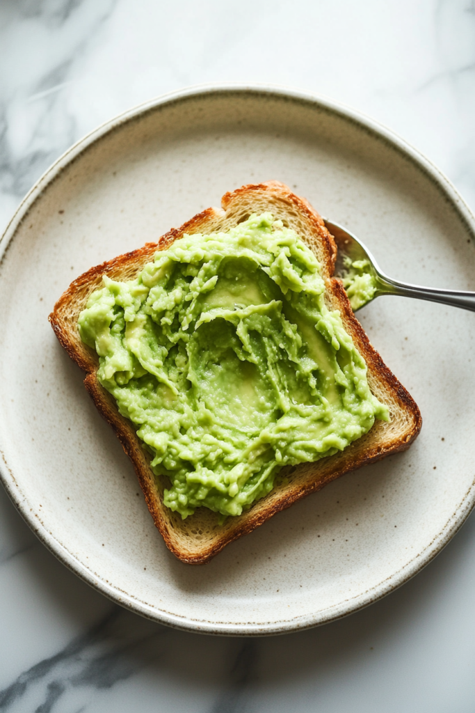 This image shows the smooth mashed avocado being spread evenly across a slice of crispy toasted bread, creating a delicious and simple avocado toast.