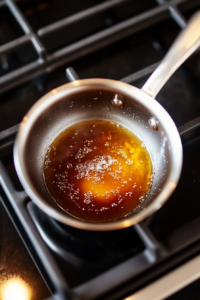 This image shows honey, sugar, and water being stirred together in a saucepan over medium heat, cooking into a slightly thickened syrup that will be poured over the cheesecake.