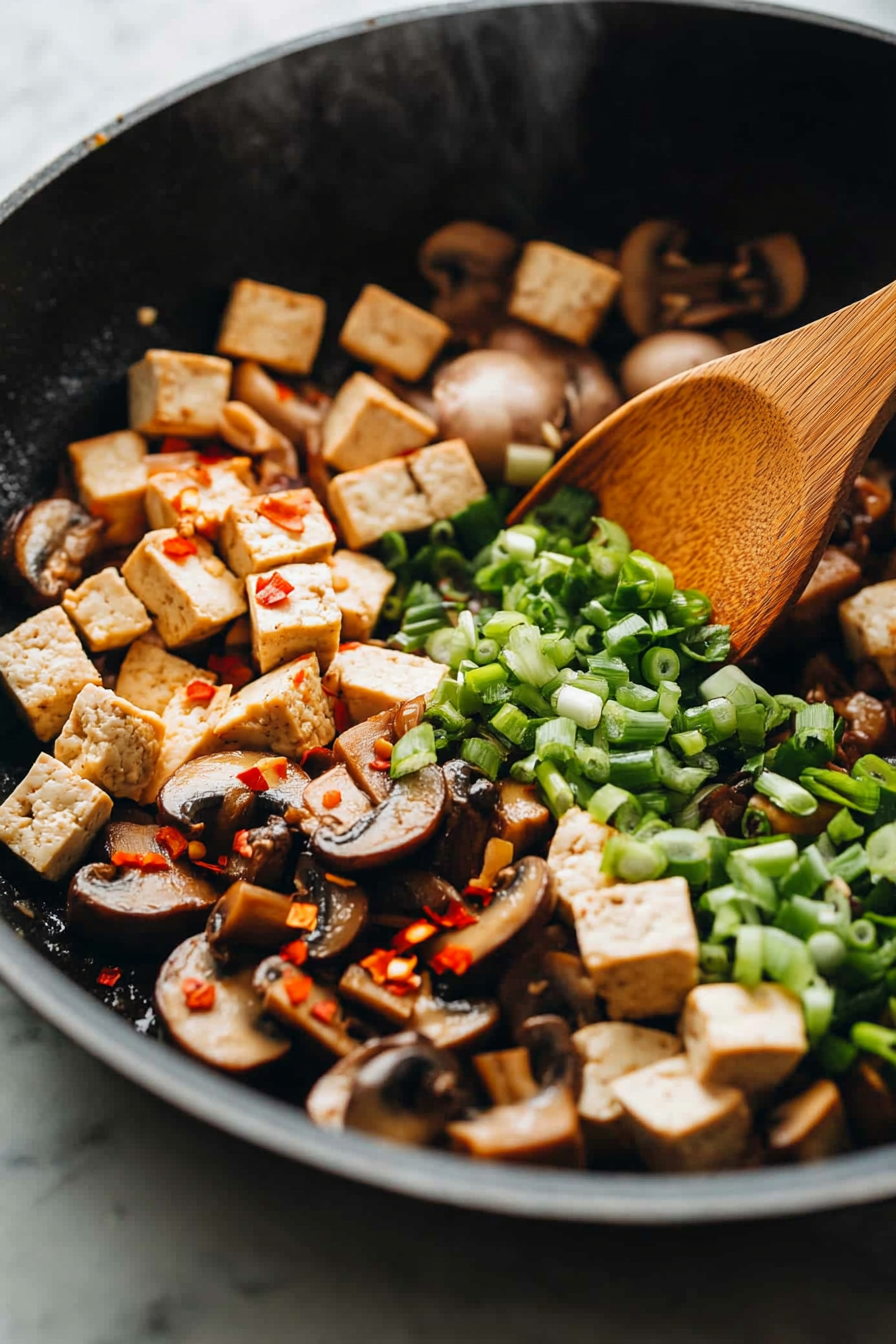 This image shows water chestnuts, garlic, ginger, red pepper flakes, and green onions being added to the tofu mixture, enhancing the flavors before the sauce is poured in.