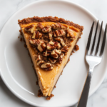 This image shows the finished sweet potato cheesecake with a golden graham cracker crust, creamy filling, and a crunchy pecan topping, beautifully presented and ready to enjoy.