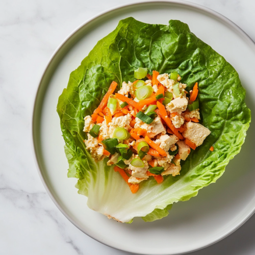 This image shows a close-up of vegan lettuce wraps filled with a savory tofu, mushroom, and water chestnut mixture, garnished with grated carrots and green onions, ready to be served as a fresh and healthy appetizer.