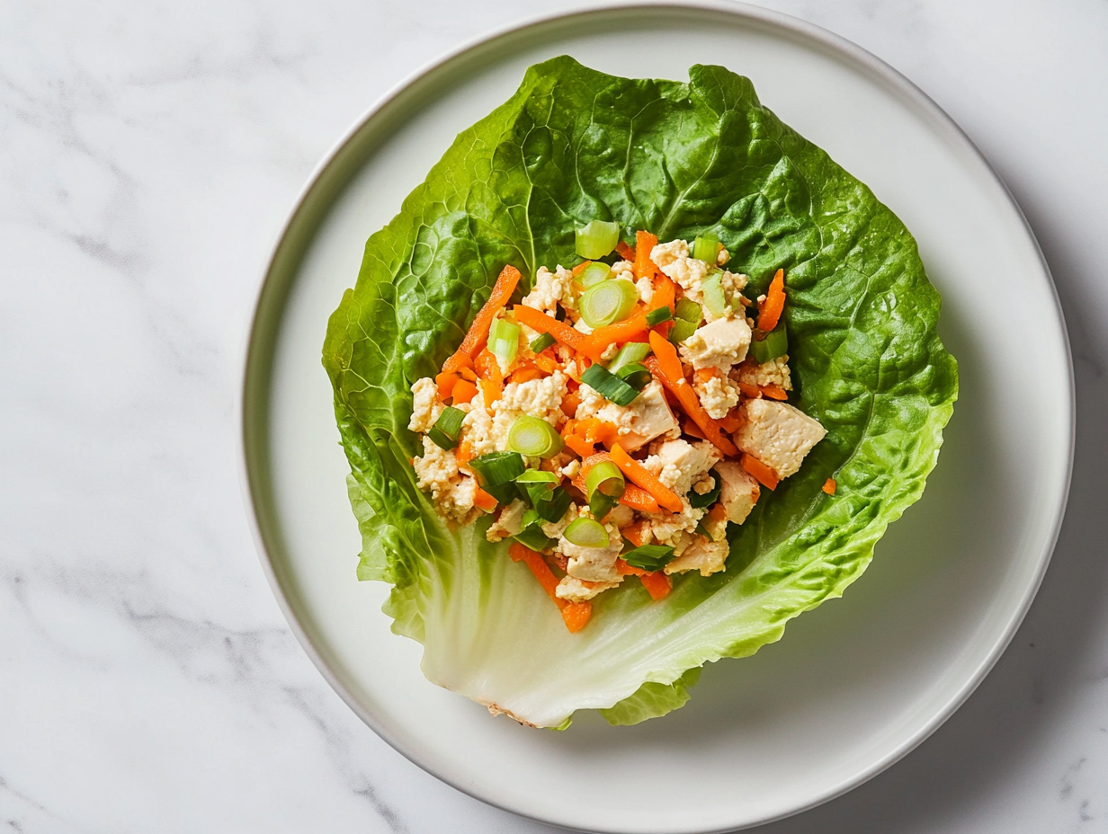 This image shows a close-up of vegan lettuce wraps filled with a savory tofu, mushroom, and water chestnut mixture, garnished with grated carrots and green onions, ready to be served as a fresh and healthy appetizer.