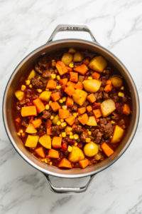 This image shows diced carrots, potatoes, sweet potatoes, corn, and pumpkin being added to the pot along with allspice, paprika, and other spices to build the rich flavor of the Jamaican soup.