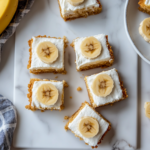 This image shows a beautiful display of banana cheesecake bars with a buttery Nilla Wafer crust, topped with optional whipped cream and fresh banana slices, showcasing a creamy and delicious dessert perfect for any occasion.