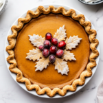 This image features a whole pumpkin pie decorated with sugared cranberries and pie crust leaves, highlighting the finished, festive dessert ready for serving.