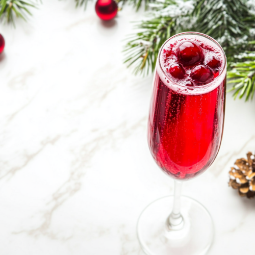 This image shows a beautifully garnished Christmas mimosa in a champagne flute, featuring sugared cranberries and a rosemary sprig, capturing the festive spirit of the holiday drink.