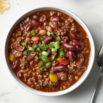 This image shows a bowl of hearty Wendy’s chili, filled with ground beef, beans, and tomatoes, and topped with a spoon for serving, ready to enjoy as a comforting and flavorful meal.