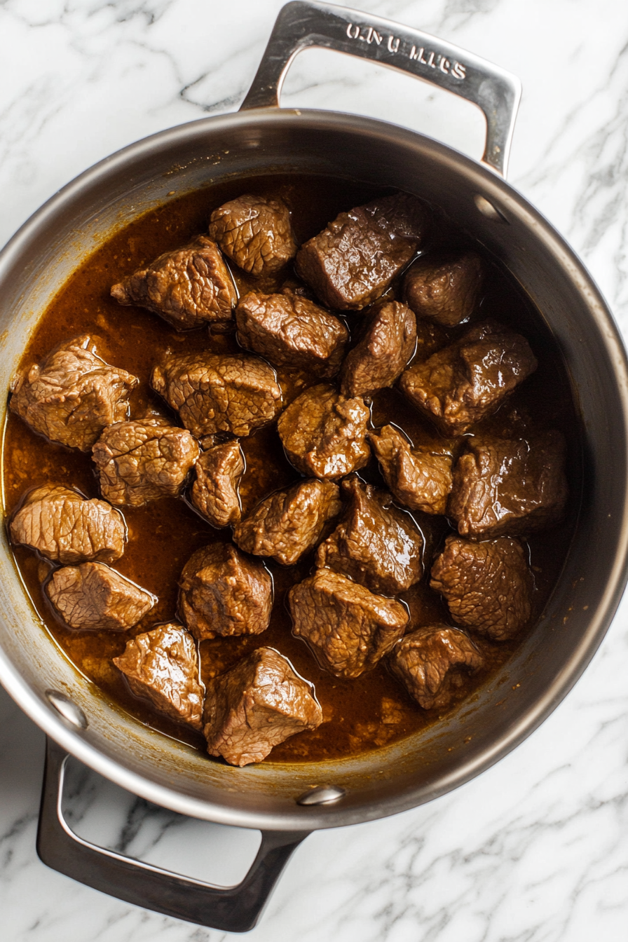 This image shows beef stew meat being browned in a large pot with vegetable oil, creating a flavorful base for the hearty Jamaican soup.