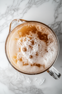 This image shows insulated gloves being used to add pieces of dry ice to the pitcher containing the root beer mixture, creating a fizzy and foggy effect.