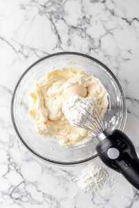 This image shows sugar, egg, and sour cream being combined in a mixing bowl, forming the soft dough for traditional Kringla cookies.