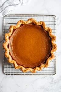 This image shows a freshly baked pumpkin pie cooling on a wire rack, allowing it to set before serving.