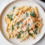 This image shows the Spinach Salmon Pasta dish, featuring creamy pasta tossed with tender flaked salmon, fresh spinach, and a light lemony cream sauce. The dish is beautifully presented and garnished with Parmesan cheese and lemon zest, making it both visually appealing and appetizing.