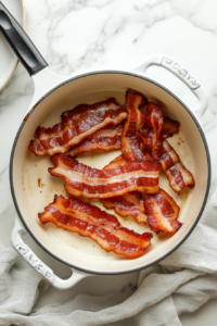 This image shows thick-cut bacon slices cooking in a soup pot, turning crispy as they release flavorful drippings for the beer cheese soup.