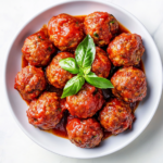 This image shows a plate of savory Italian meatballs cooked in a crockpot, topped with a rich marinara sauce. The dish is garnished and ready to be served as a comforting main course.