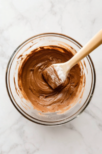 This image shows all-purpose flour being gently folded into the Nutella and egg mixture, ensuring a smooth and fully mixed cake batter.