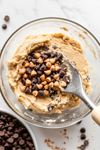 This image shows chocolate chips and chopped hazelnuts being folded into the Nutella cookie dough, adding extra crunch and sweetness to the cookies.