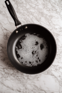 This image shows olive oil heating in a large pot, getting ready to brown the ground beef for Wendy's chili recipe. The oil is gently shimmering over medium-high heat.