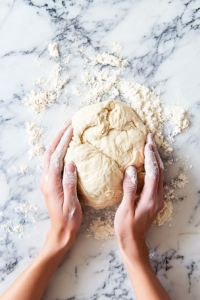 This image shows bread dough being kneaded on a floured surface until it becomes smooth and elastic, preparing it for the first rise.