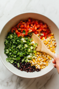 This image shows all the cowboy caviar ingredients being tossed together in a large mixing bowl, combining the beans, corn, peppers, and Rotel.