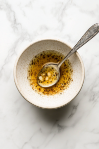 This image shows melted butter, minced garlic, Italian seasoning, paprika, salt, and pepper being mixed together in a bowl to create a rich and flavorful garlic butter sauce for coating the chicken breasts.