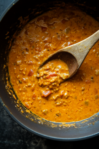 This image shows coconut milk and chicken-style liquid stock being poured into the saucepan, creating a creamy and flavorful base for the Thai red curry vegetables.