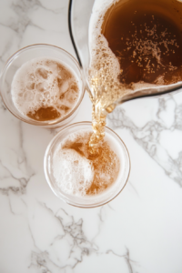 This image shows homemade root beer being ladled into cups, showcasing the fizzy and frothy texture of the drink as it’s served.