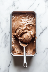 This image shows the thick and fluffy Nutella ice cream mixture being poured into a loaf tin, spread evenly and ready for freezing.