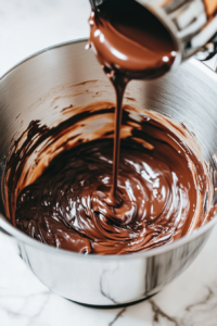 This image shows warm Nutella being poured into the beaten eggs in the stand mixer, creating a smooth and fluffy Nutella cake batter as it is mixed.