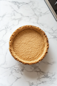 This image shows graham cracker crust being pressed into a pie dish, preparing it to chill before adding the filling.