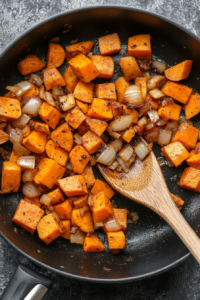 This image shows onion wedges and crushed garlic being sautéed in a saucepan until softened, preparing the fragrant base for the Thai red curry vegetables.