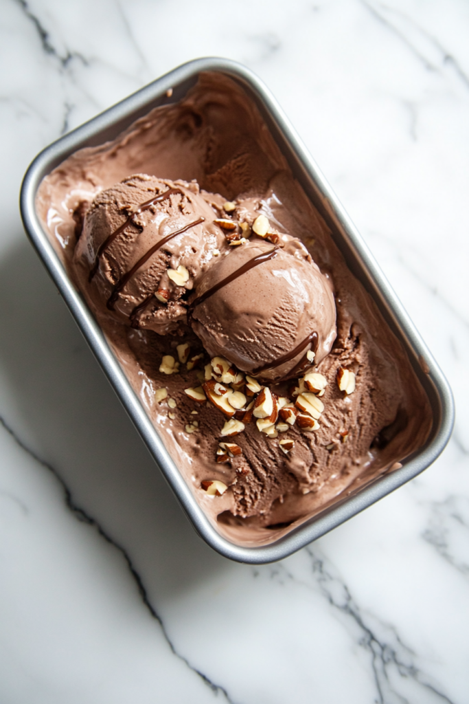 This image shows creamy homemade Nutella ice cream being served in bowls, garnished with chopped hazelnuts and a drizzle of chocolate sauce for an extra indulgent treat.