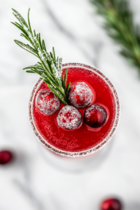 This image shows the finished Christmas mimosa being served in a champagne flute, garnished with sugared cranberries and rosemary, ready for a holiday toast.