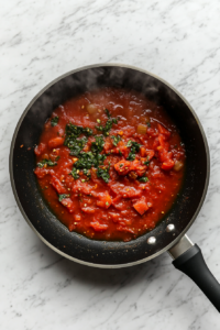 This image shows the tomato sauce simmering with crushed tomatoes, basil, and parsley, creating a flavorful and thickened sauce for the ratatouille.