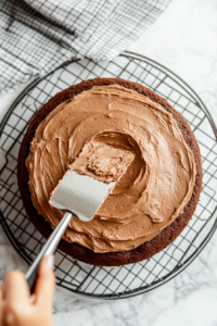 This image shows a generous layer of Nutella being spread over the cooled chocolate Nutella cake, adding a rich and indulgent frosting.