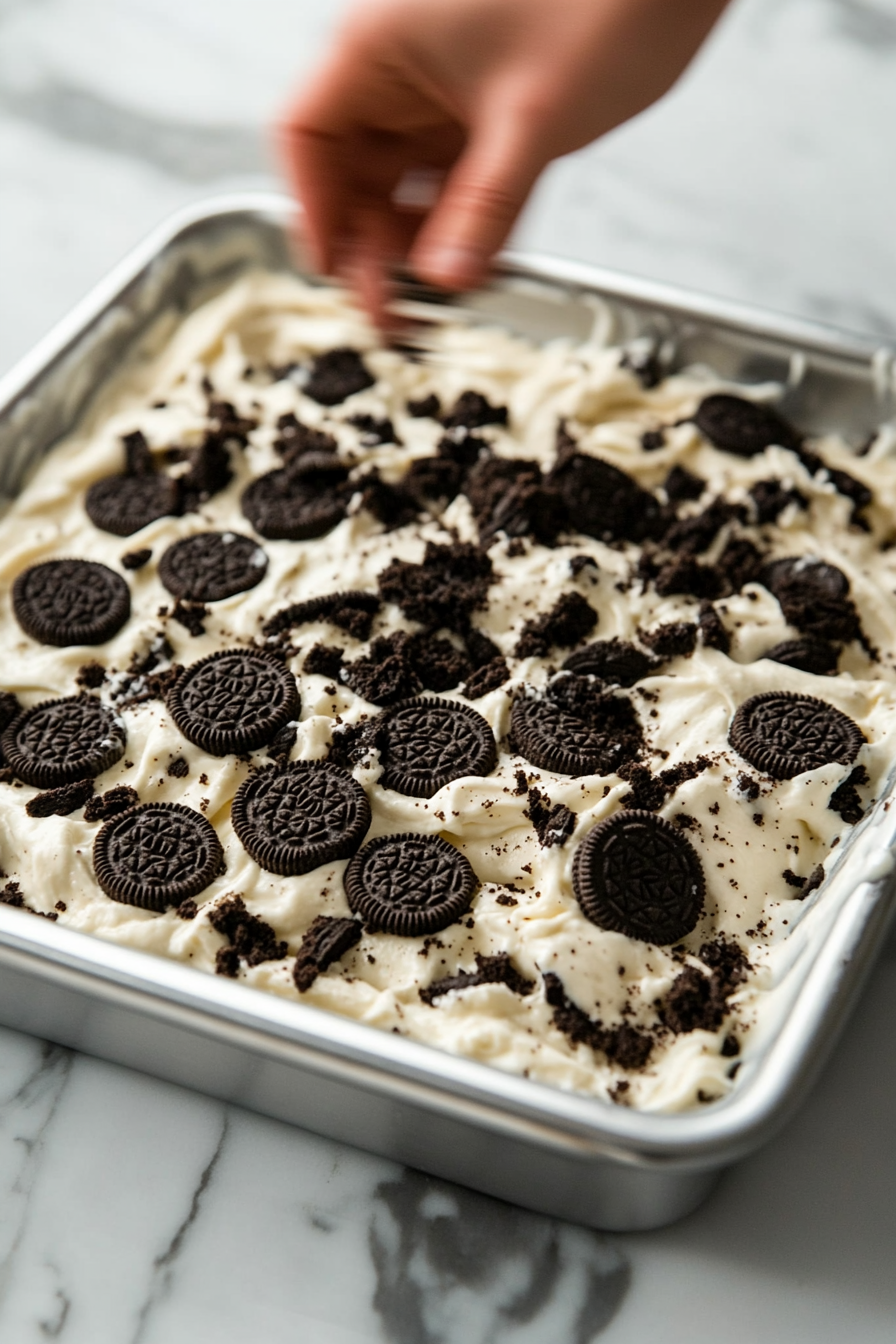 This image shows the remaining chopped Oreos being sprinkled on top of the cheesecake layer, ready to be baked in the oven for a delicious dessert.