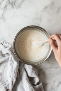 This image shows calcium chloride solution and mesophilic culture being carefully stirred into the warmed milk, beginning the process of curd formation for homemade cheese curds.