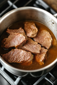 This image shows thinly sliced roast beef being gently warmed in beef-flavored water on the stove, ensuring it stays tender without overcooking.