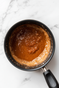 This image shows brown sugar, cinnamon, and cream being whisked into melted butter to create a smooth and sweet dipping sauce.