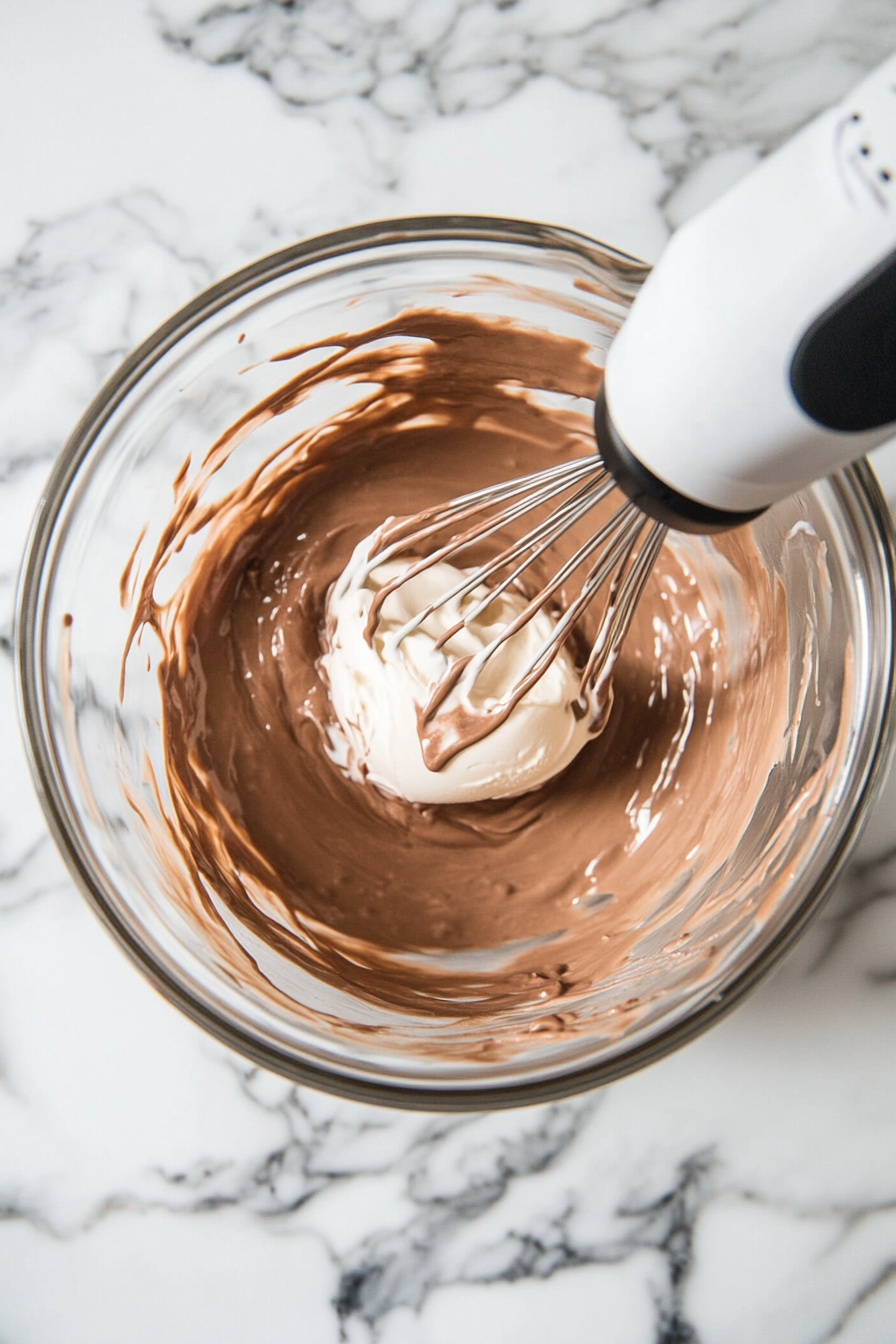 This image shows the Nutella ice cream mixture being whisked in a stand mixer until it reaches a thick, mousse-like consistency, ready to be transferred to a tin for freezing.