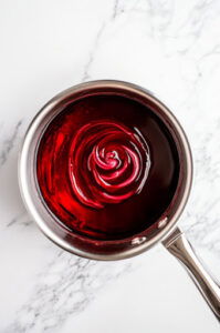 This image shows the saucepan being removed from heat and food coloring being added to the hot candy syrup.