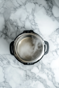 A top-down view of a 6-quart Instant Pot on a clean kitchen countertop with a white marble cooktop background. Inside the pot, 2 cups of rinsed white jasmine rice are being added, followed by 2 cups of water. The lid is beside the pot, ready to be secured.