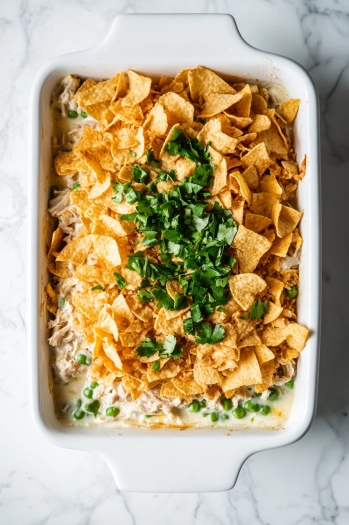 Top-down view of mixed tuna casserole ingredients being spread evenly into a greased 9x13 baking dish. The mixture is smoothed out, ready for the potato chip topping before baking.