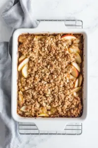 Top-down view of the golden-brown apple crisp fresh out of the oven, cooling on a wire rack with bubbling edges and a crispy oat topping.