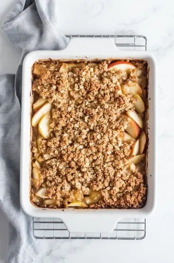 Top-down view of the golden-brown apple crisp fresh out of the oven, cooling on a wire rack with bubbling edges and a crispy oat topping.