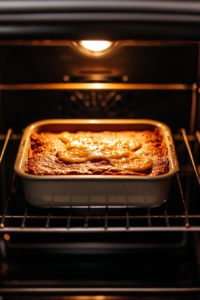 A top-down view of the baking dish placed in a preheated oven set to 350°F (175°C). The cake is baking on the middle rack of the oven. The scene captures the even rise of the cake with the oven timer set for 30-40 minutes.