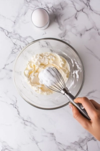 Top-down view of egg whites being gently folded into the cake batter with a rubber spatula in a large mixing bowl.