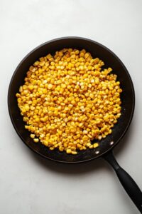 Top-down view of the skillet as the corn becomes golden and slightly charred after 8-10 minutes of cooking. The caramelized corn is combined with tender jalapeño and garlic, showcasing rich color and texture.