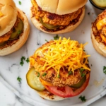 This image shows juicy chicken burgers topped with melted cheddar cheese, crispy bacon, fresh vegetables, and ranch dressing, served on toasted buns.