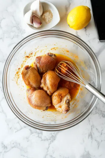 This image shows chicken thighs coated in a golden curry marinade with visible spices like turmeric, cumin, and paprika in a large bowl.