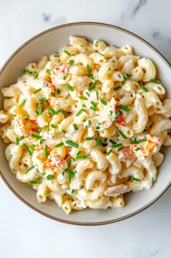 Top-down view of crab pasta salad garnished with freshly chopped chives, served in a large bowl on a white marble surface, ready to be enjoyed